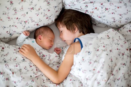 Téléchargez les photos : Beau garçon, embrassant avec tendresse et soin son petit frère nouveau-né à la maison. Famille amour bonheur concept - en image libre de droit