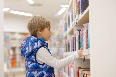 Foto de Niño inteligente, chico de escuela, educándose en una biblioteca, pidiendo prestado libros para leer - Imagen libre de derechos