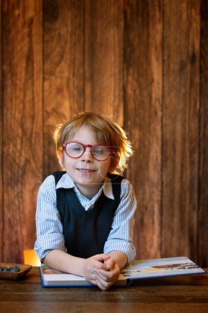 Foto de Lindo niño, niño con gafas, leyendo un libro en casa, tiro al estudio - Imagen libre de derechos