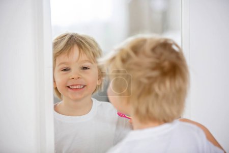 Foto de Lindo niño, rubio, cepillándose los dientes en casa, aislado - Imagen libre de derechos