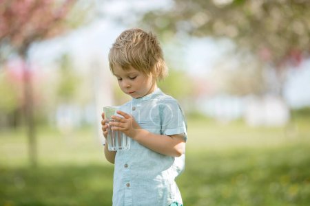 Photo for Beautiful blond child, boy, drinking water in the park on a hot summer day - Royalty Free Image