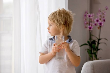 Téléchargez les photos : Petit garçon sucré, boire de l'eau à la maison, boire une boisson saine - en image libre de droit