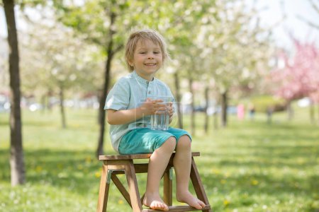 Foto de Hermoso niño rubio, niño, beber agua en el parque en un día caluroso de verano - Imagen libre de derechos