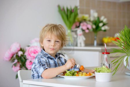 Foto de Niño pequeño, niño rubio, comer verduras hervidas, brócoli, papas y zanahorias con carne de pollo frito en casa, comida sana casera recién cocinada - Imagen libre de derechos