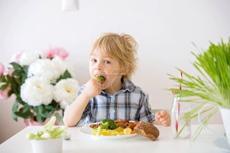 Photo for Little toddler child, blond boy, eating boiled vegetables, broccoli, potatoes and carrots with fried chicken meat at home, chewing fresh salad - Royalty Free Image