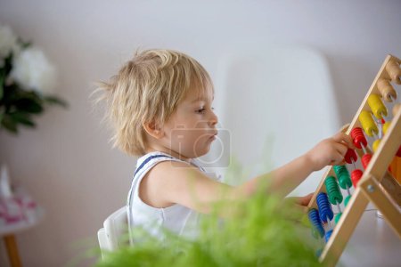 Foto de Dulce niño pequeño, niño rubio, aprender matemáticas en casa con ábaco colorido, beber jugo recién hecho - Imagen libre de derechos