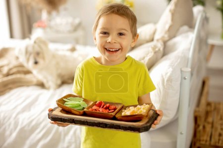 Foto de Lindo niño preescolar, niño, comer frutas secas en casa, fresas, melón, piña en un plato - Imagen libre de derechos