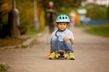 Foto de Niño pequeño, niño pequeño, monopatín en el parque por primera vez, tratando de - Imagen libre de derechos