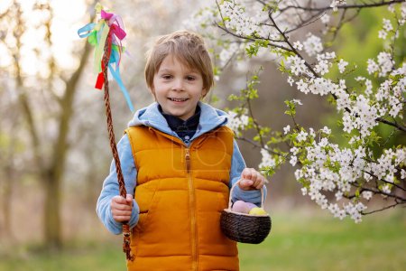 Photo for Beautiful blond child, boy, holding twig, braided whip made from pussy willow, traditional symbol of Czech Easter used for whipping girls and basket with eggs in park - Royalty Free Image
