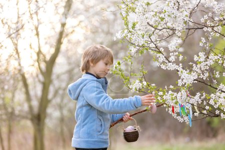 Foto de Beautiful blond child, boy, holding twig, braided whip made from pussy willow, traditional symbol of Czech Easter used for whipping girls and basket with eggs in park - Imagen libre de derechos