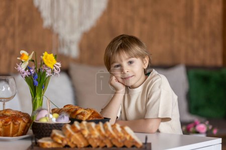 Foto de Lindo niño preescolar, niño, sosteniendo bollo brioche dulce para Pascua, pan dulce tradicional horneado con almendras, nueces y azúcar, hogar - Imagen libre de derechos