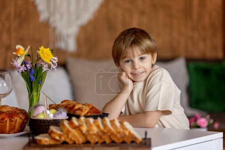 Foto de Lindo niño preescolar, niño, sosteniendo bollo brioche dulce para Pascua, pan dulce tradicional horneado con almendras, nueces y azúcar, hogar - Imagen libre de derechos