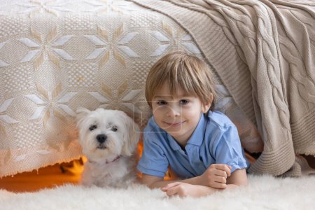 Little preschool child, hiding under the bed with his dog,  holding flashlight at home