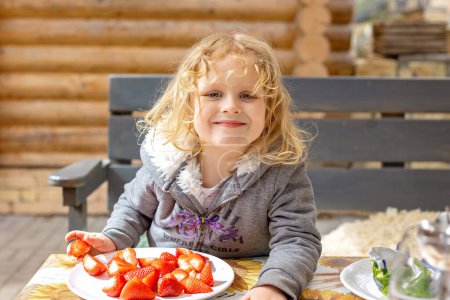 Photo for Children, kids, eating strawberries outdoors on a sunny spring day - Royalty Free Image