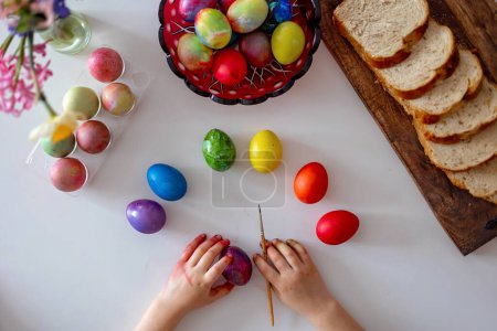 Foto de Beatiful niño rubio, niño, colorear y pintar huevos para Pascua en casa, preparándose para las vacaciones - Imagen libre de derechos