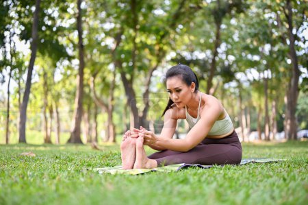 Photo for Attractive and charming Asian woman in sportswear stretching and practicing yoga in the beautiful green garden. Seated Forward Fold - Royalty Free Image