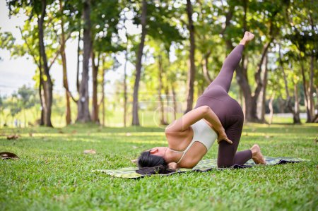 Téléchargez les photos : Belle femme asiatique en vêtements de sport étirement et pratique du yoga dans le beau jardin vert - en image libre de droit