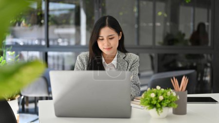 Attractive beautiful young Asian businesswoman or female office worker focusing on her project, working at her desk in the office.