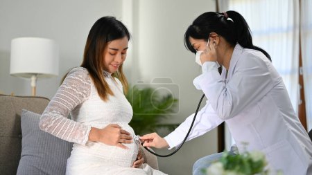 Professionelle asiatische Ärztin oder Geburtshelferin, die dem Herzschlag des Babys mit ihrem Stethoskop zuhört, untersucht ihre Patientin in ihrer Praxis. Antenatalversorgungskonzept