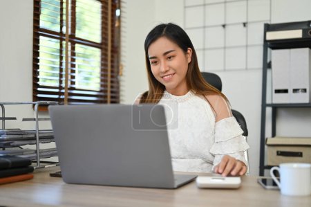 Téléchargez les photos : Attrayant millénaire asiatique femme d'affaires travaillant à son bureau, en utilisant un ordinateur portable pour gérer ses tâches commerciales. - en image libre de droit