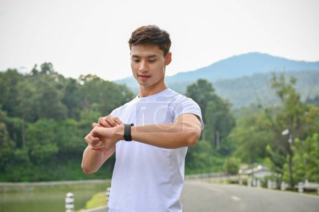 Foto de Primer plano, guapo y saludable joven asiático en ropa deportiva comprobar su ritmo cardíaco y calorías quemadas de correr en su reloj inteligente. Concepto de actividad y tecnología - Imagen libre de derechos