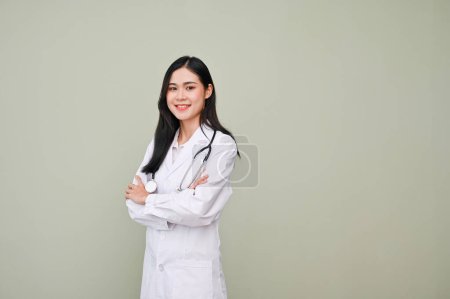 Téléchargez les photos : Jeune médecin asiatique professionnelle et réussie en uniforme avec bras stéthoscopiques croisés, souriants, caméra de regard, debout sur fond gris. docteur, docteur, dentiste, infirmière - en image libre de droit