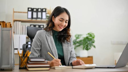 Photo for Charming and professional millennial Asian businesswoman or female manager working at her desk, taking notes on her schedule book. - Royalty Free Image