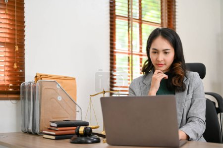 Professional and thoughtful millennial Asian female lawyer or business legal consultant hand on chin while pensively thinking and working on her case, looking at laptop screen.
