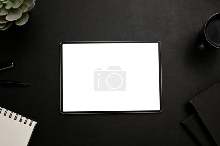 Espace de travail moderne avec tablette écran vierge maquette entourée d'accessoires et de papeterie sur fond noir. vue du dessus, plan plat