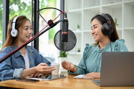 Photo for Two attractive and professional young Asian female radio host working together in the studio, enjoys running their podcast show as a team. - Royalty Free Image