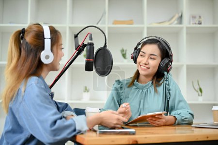 Photo for Happy and cheerful young Asian female radio guest enjoys talking with a professional female radio host in the studio. podcast and broadcast concept. - Royalty Free Image