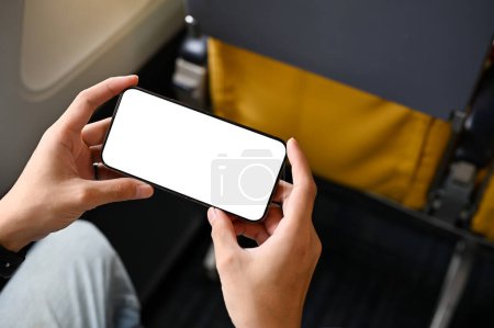 Photo for Close-up image, A male passenger using his smartphone during a flight, watching movie or video. phone white screen mockup. Technology and transportation concept - Royalty Free Image
