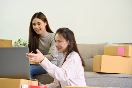 Foto de Dos jóvenes asiáticas pequeñas empresarias de comercio electrónico que trabajan juntas, revisando sus pedidos de venta en línea en un ordenador portátil. - Imagen libre de derechos