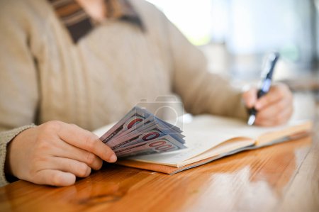 Eine Frau, die ihre Einnahmen und Ausgaben in einem Buch abrechnet oder ihr monatliches Budget verwaltet, verwaltet Bargeld. zugeschnittenes und Nahaufnahme-Bild