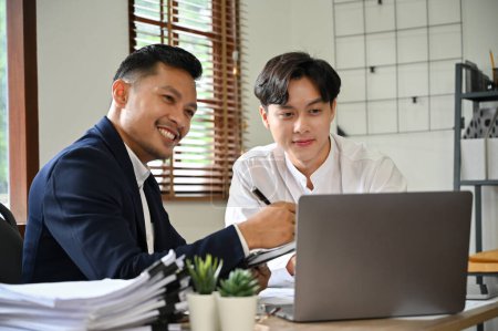 Photo for Professional and smart Asian male financial counselors analyzing financial data on the report, looking at laptop screen, meeting and working together in the office. - Royalty Free Image