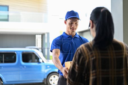 Téléchargez les photos : Livreur professionnel en uniformes bleus remettant le colis au client debout devant son van - en image libre de droit