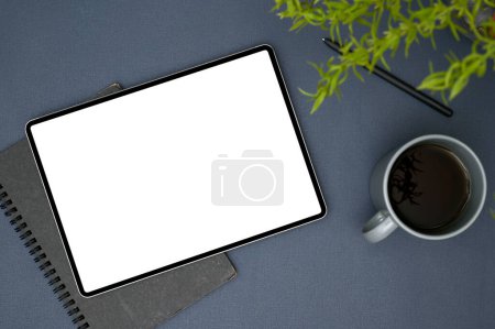Téléchargez les photos : Espace de travail moderne avec tablette numérique portable écran blanc maquette, stylo, bloc-notes en spirale, tasse à café et plante de décoration sur fond bleu de table. vue de dessus - en image libre de droit