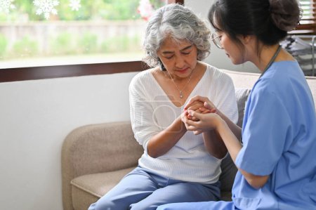 Photo for Caring young Asian female doctor or nurse holding an aged female's hands to comfort and support her patient's feeling. cheering up, reassuring, togetherness. - Royalty Free Image