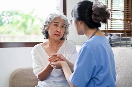Photo for An elderly woman is reassured by a doctor. Caring and kind young Asian female doctor or nurse holding an aged female's hands to comfort and support her patient's feeling. - Royalty Free Image