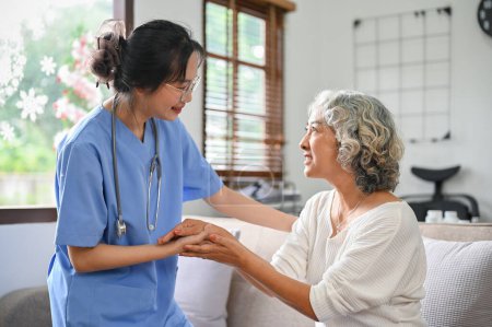 Téléchargez les photos : Soigneuse et gentille jeune femme asiatique médecin ou infirmière tenant les mains d'une femme âgée pour le confort et le soutien tout en vérifiant sa santé. Une femme âgée est rassurée par un médecin. - en image libre de droit