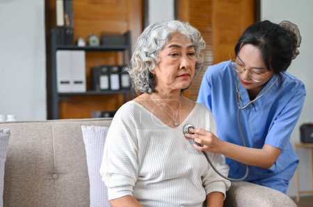 Photo for Sick and depressed 60-year-old elderly retire woman sitting on sofa while her doctor checking up, listening to heartbeat sound with stethoscope. - Royalty Free Image