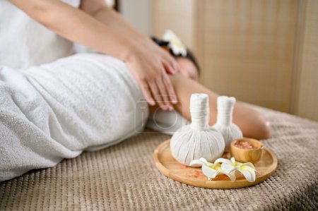 Photo for Thai spa concept, Spa herbal balls or massage stamps and spa salt on massage table with a young lady receiving massage on the massage table. - Royalty Free Image