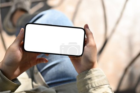 Photo for Above view, A female holding a smartphone in horizontal position, watching video, playing mobile game. phone white screen mockup - Royalty Free Image
