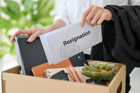 Photo for A businesswoman with a resignation letter in her hand and her stuff in a cardboard box. moving, quit a job, unemployment, career failure. close-up image - Royalty Free Image