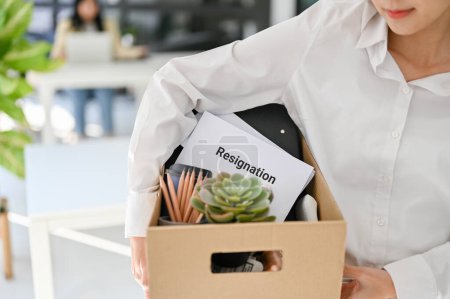 Photo for Cropped shot of an Asian female office worker carrying a cardboard box with her personal stuff and resignation letter. - Royalty Free Image
