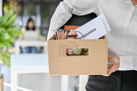 Foto de Cropped shot of a female office worker carrying a cardboard box with her personal stuff and resignation letter. quitting a job, leaving a job - Imagen libre de derechos