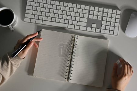Téléchargez les photos : Vue de dessus d'une femme travaillant à son bureau, faisant ses devoirs, écrivant quelque chose sur son carnet en spirale. pages blanches vides. - en image libre de droit