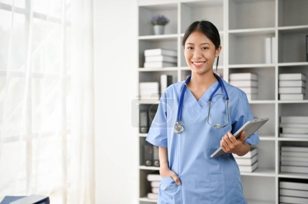 Photo for Portrait of young Asian medical student smiling and standing in the study room while holding tablet on her hand - Royalty Free Image