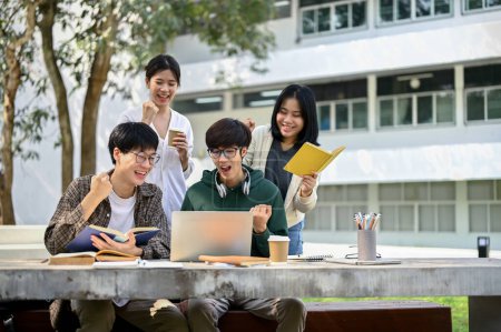 Group off cheerful young Asian college students looking at laptop screen, rejoicing, and celebrating their school project success or exam score together at a campus park.