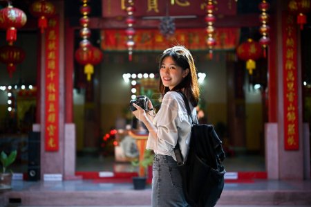 Attractive and smiling young Asian female tourist sightseeing and visiting a beautiful Chinese temple in Chiang Mai. Solo travel and historical sightseeing trip concept